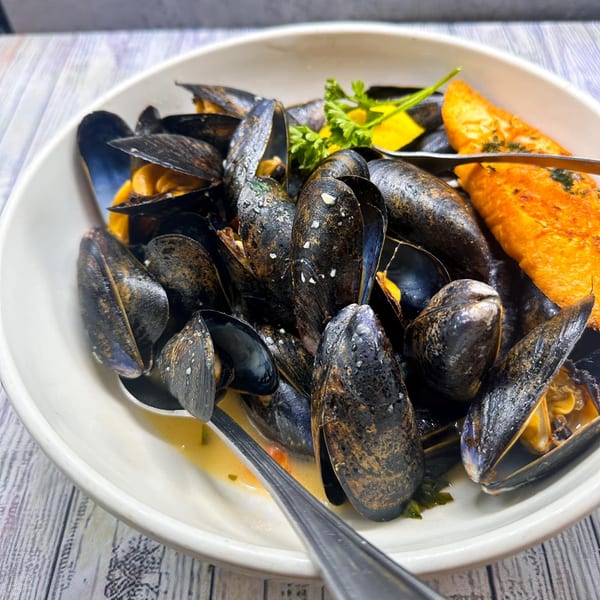 A white bowl filled with steamed mussels, garnished with parsley and lemon, served with toasted bread.