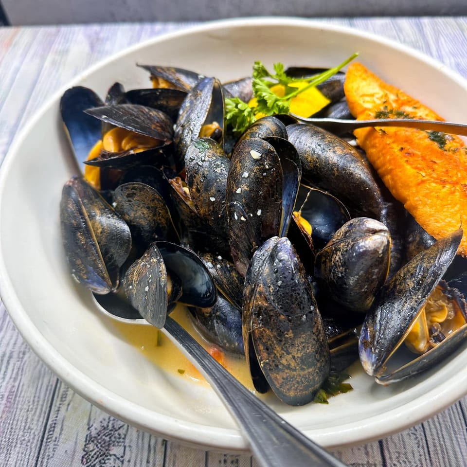 A white bowl filled with steamed mussels, garnished with parsley and lemon, served with toasted bread.