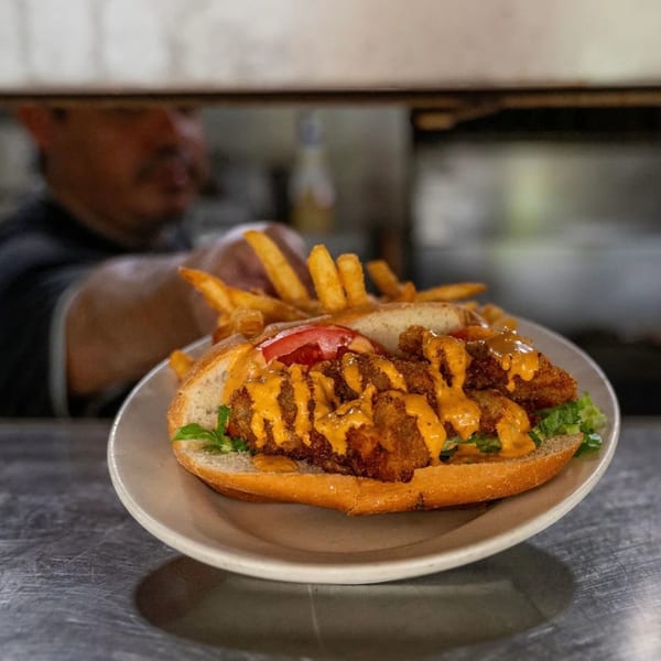 Crispy fried seafood po'boy with sauce, lettuce, tomato, and fries on a plate.