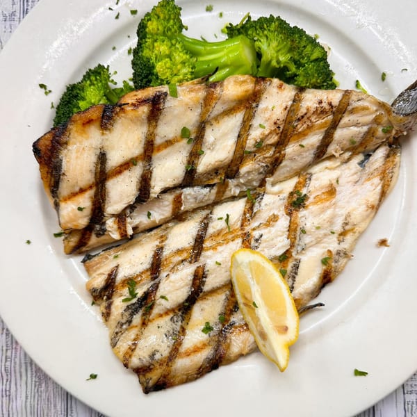 Grilled fish fillets with char marks, served with green broccoli florets and a lemon wedge.