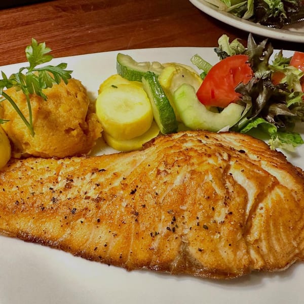 A perfectly cooked salmon fillet with mashed sweet potatoes, zucchini, squash, and a side salad.