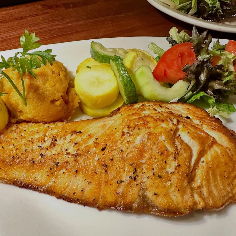 A perfectly cooked salmon fillet with mashed sweet potatoes, zucchini, squash, and a side salad.