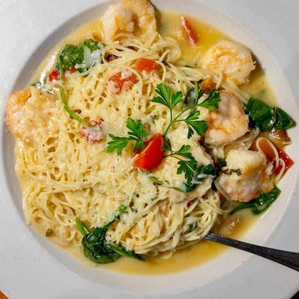 Shrimp scampi with angel hair pasta, spinach, tomatoes, and parsley in a white bowl.