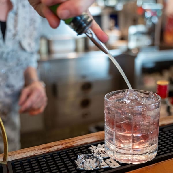 A bartender pours a pink cocktail into a glass filled with ice at The Fish House.