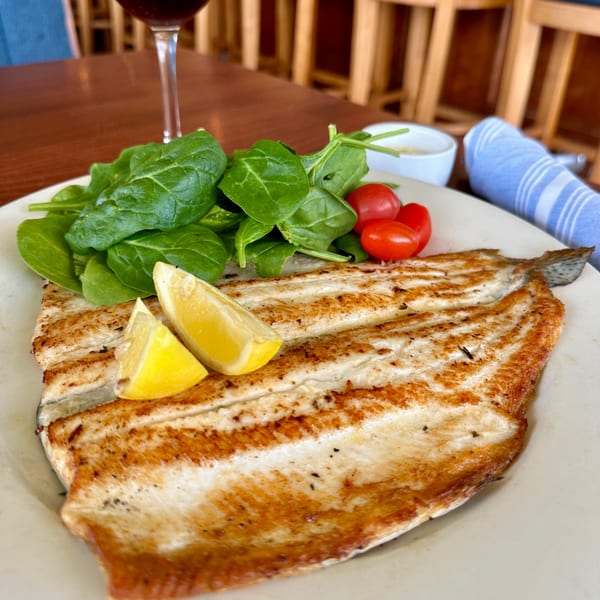 Grilled fish fillet with lemon wedges, spinach, and cherry tomatoes on a white plate.