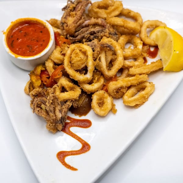 Crispy fried calamari rings and tentacles with a side of red marinara sauce and a lemon wedge.